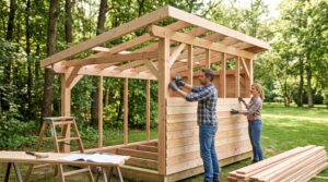 Au milieu du jardin, un homme et une femme vissent le bardage sur une ossature bois près de leurs plans.